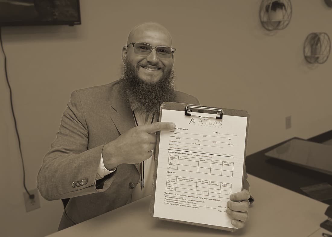 A team member in a blazer, smiling, pointing to an Atlas Empowered form on a clipboard.