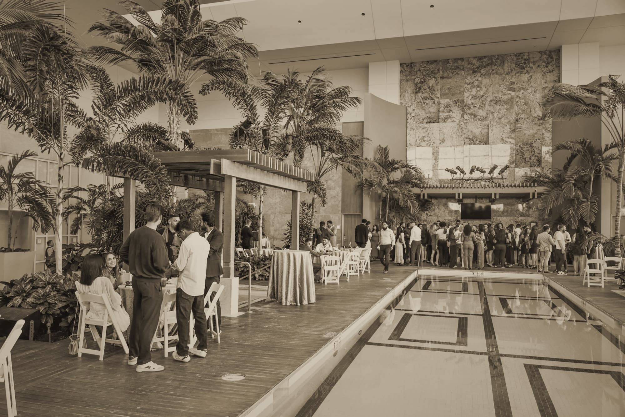 Dozens of team members gathered around an indoor pool under palm trees at a leadership conference.