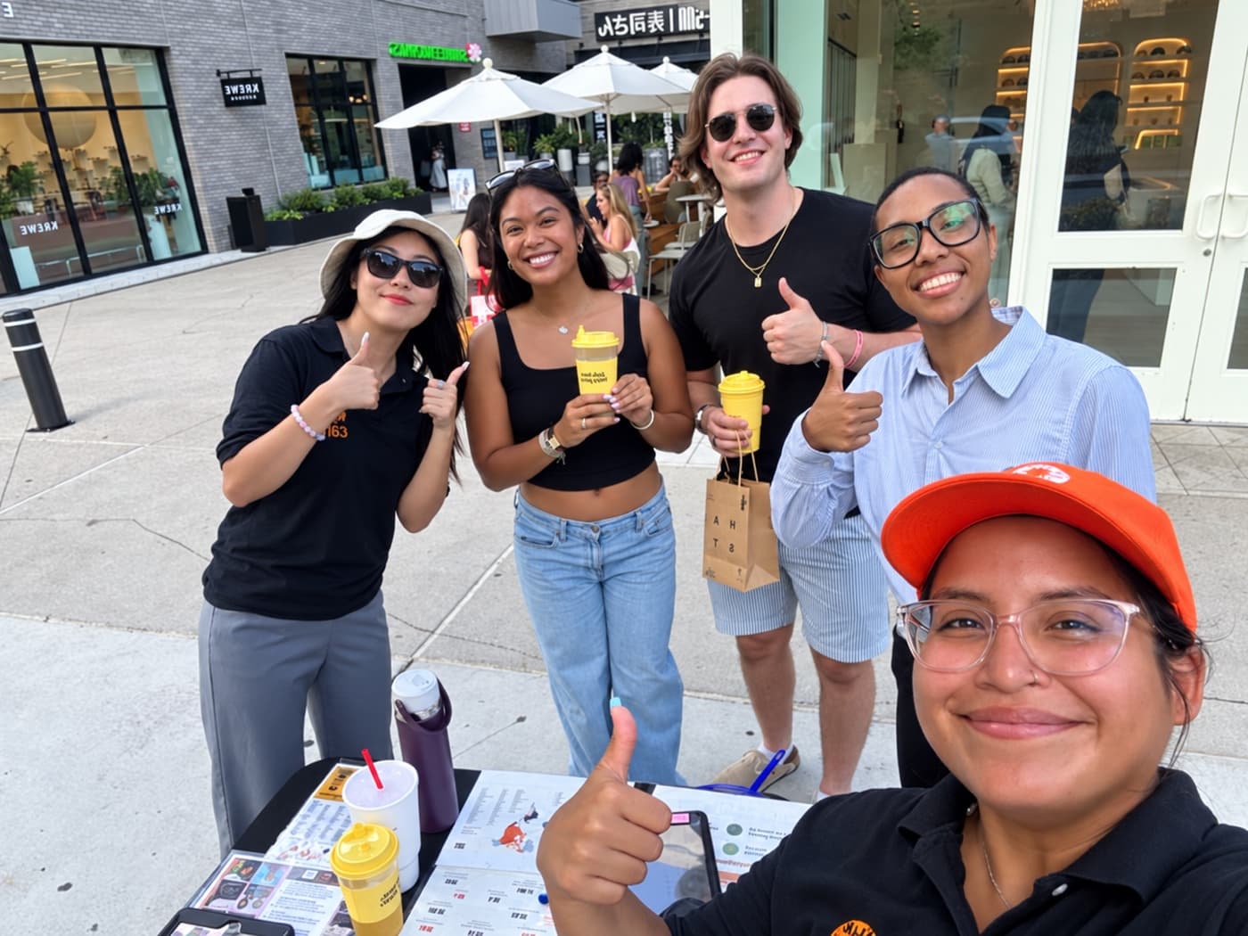 Four supporters giving thumbs up beside a fundraiser at a sidewalk table