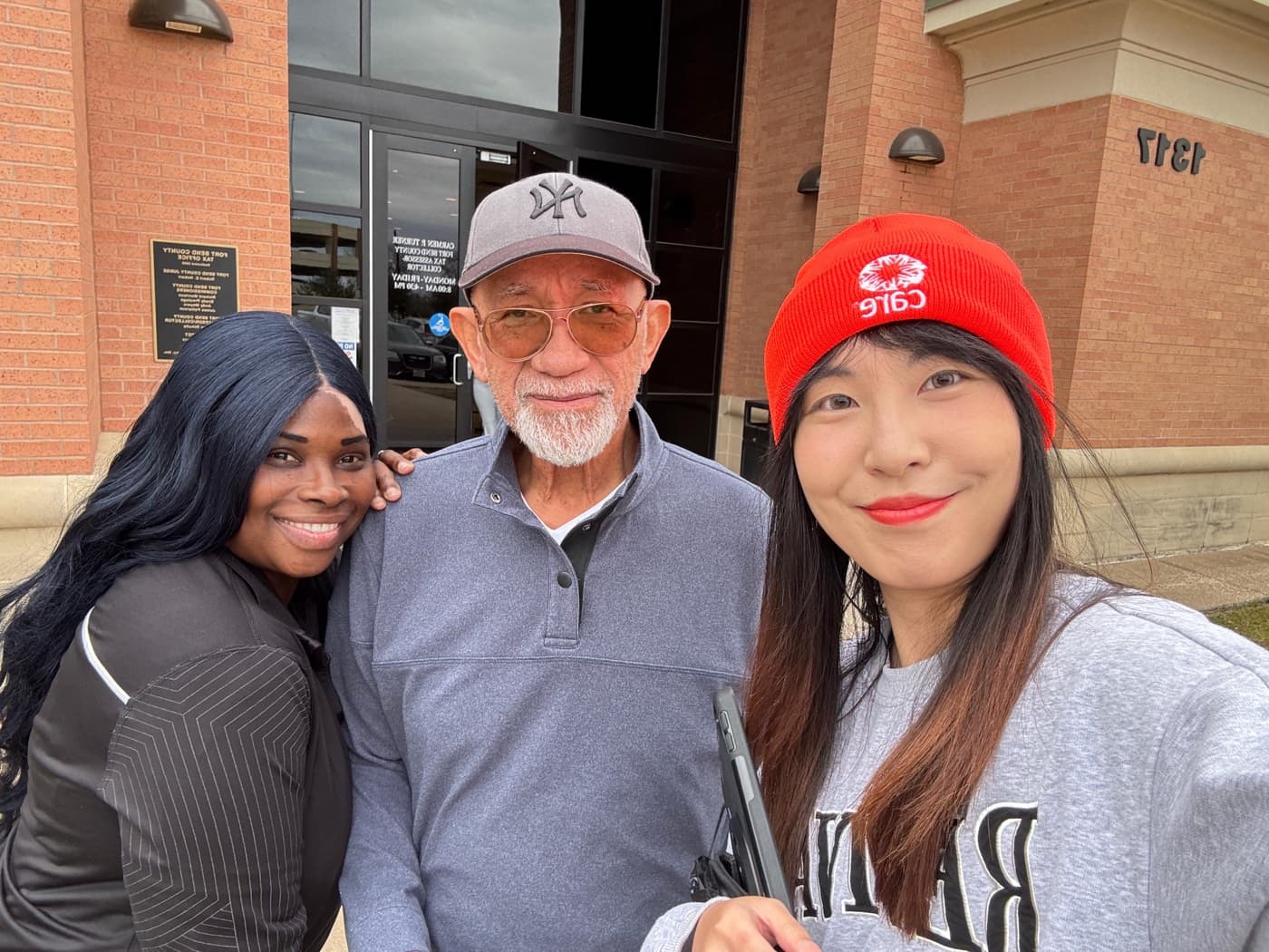 Two fundraisers and a supporter smiling outside a brick office building