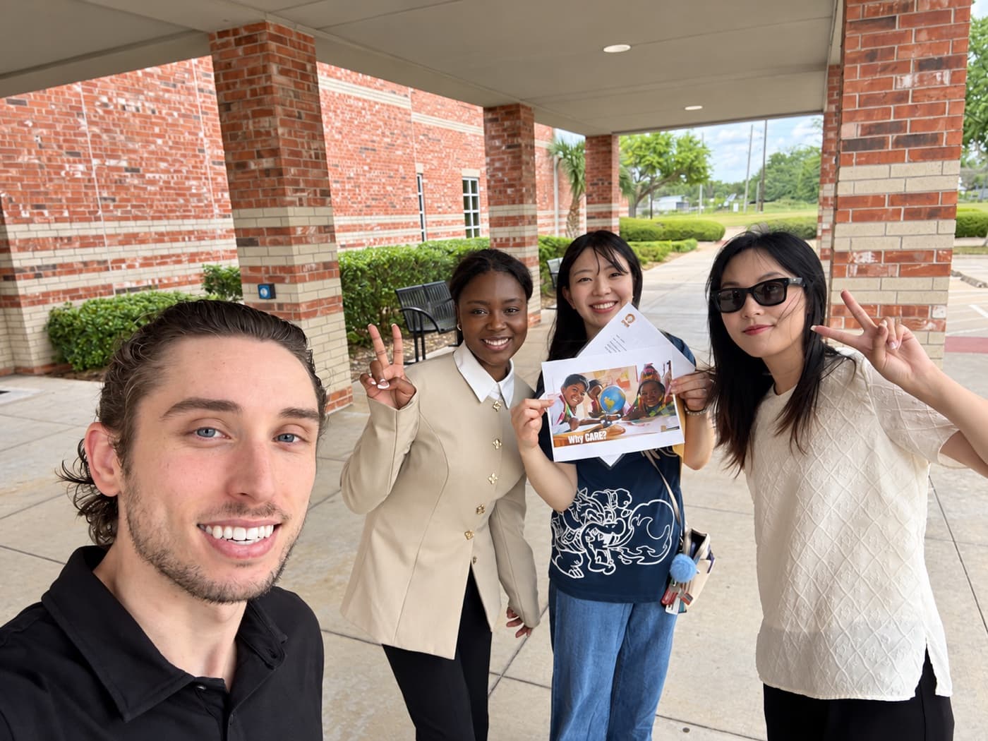 A fundraiser and three supporters flashing peace signs under a brick colonnade, one holding a brochure
