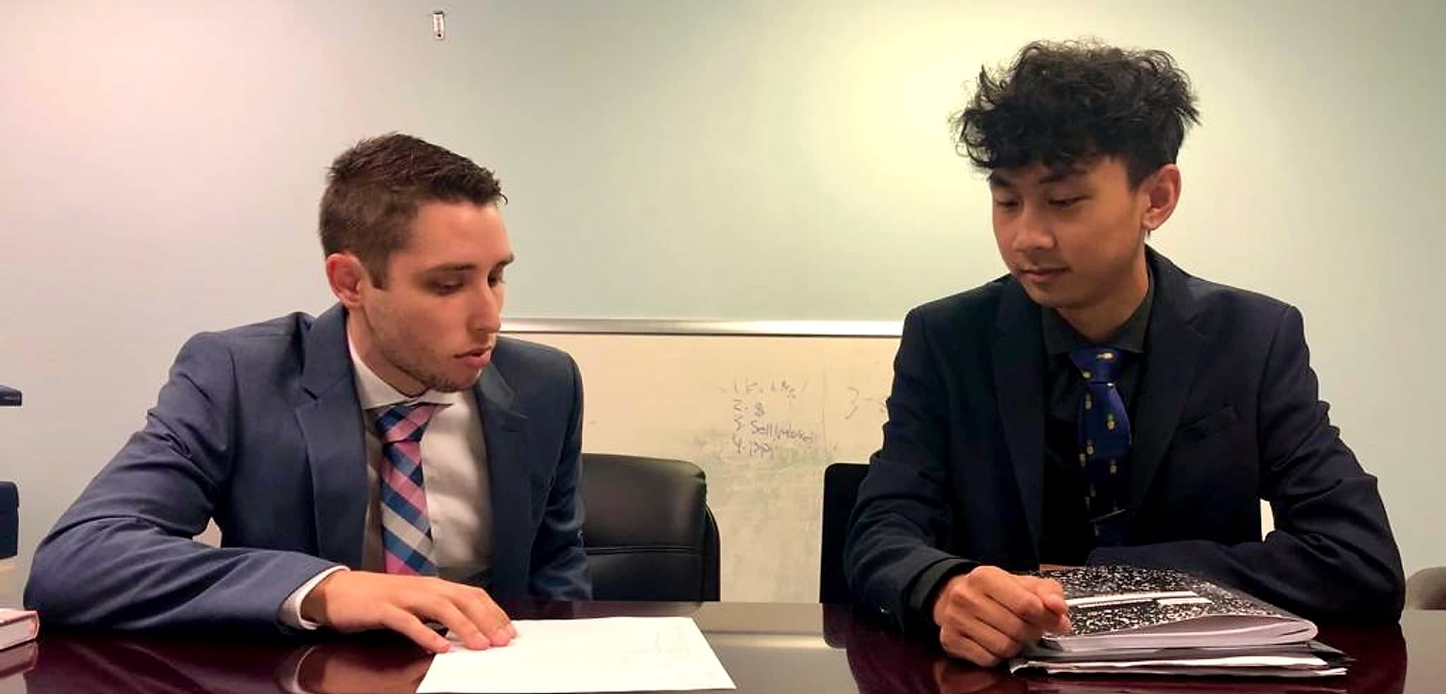 Zach Pyron, on the left, reviewing papers at a conference table beside another man in a suit.