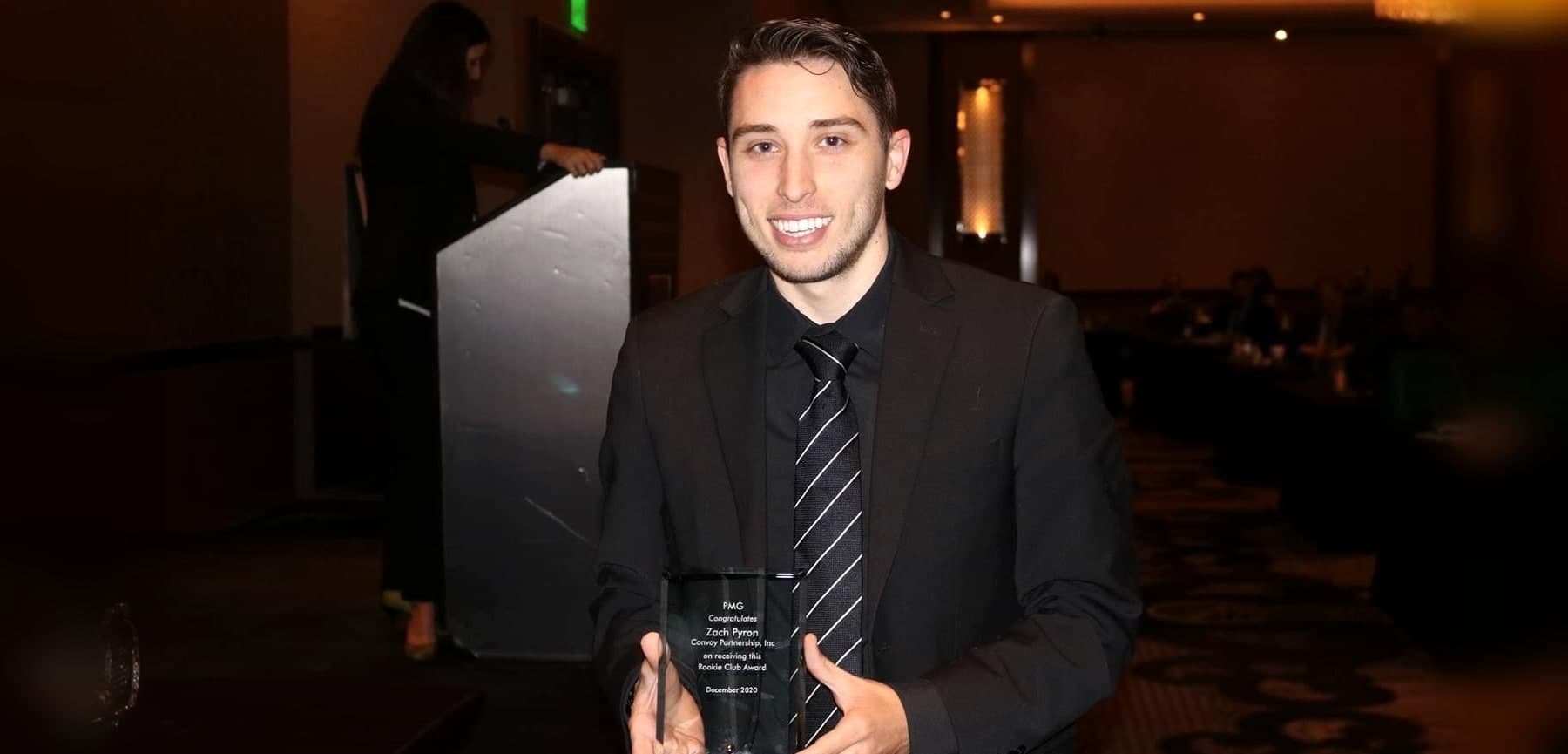 Zach Pyron smiling in a ballroom, holding a glass sales award from PMG.