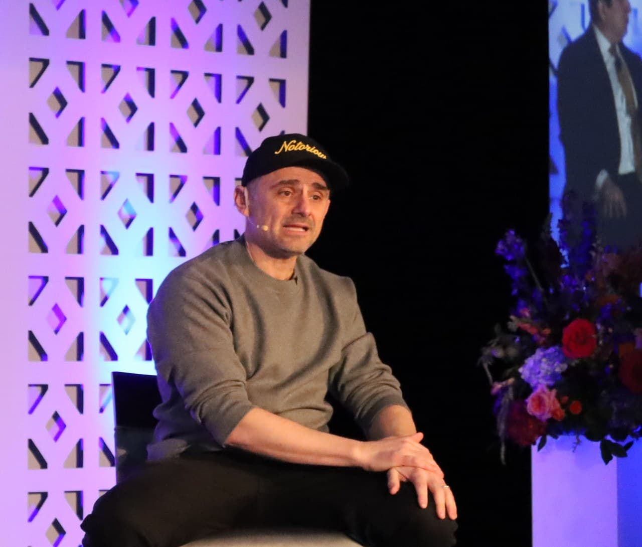 Gary Vaynerchuk seated on a stool on stage, speaking at a company conference.