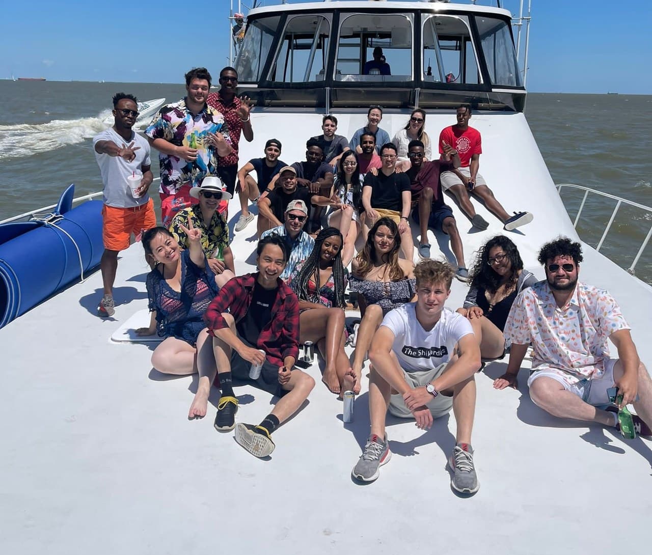 A big group of teammates sitting together on the bow of a boat on a sunny day.