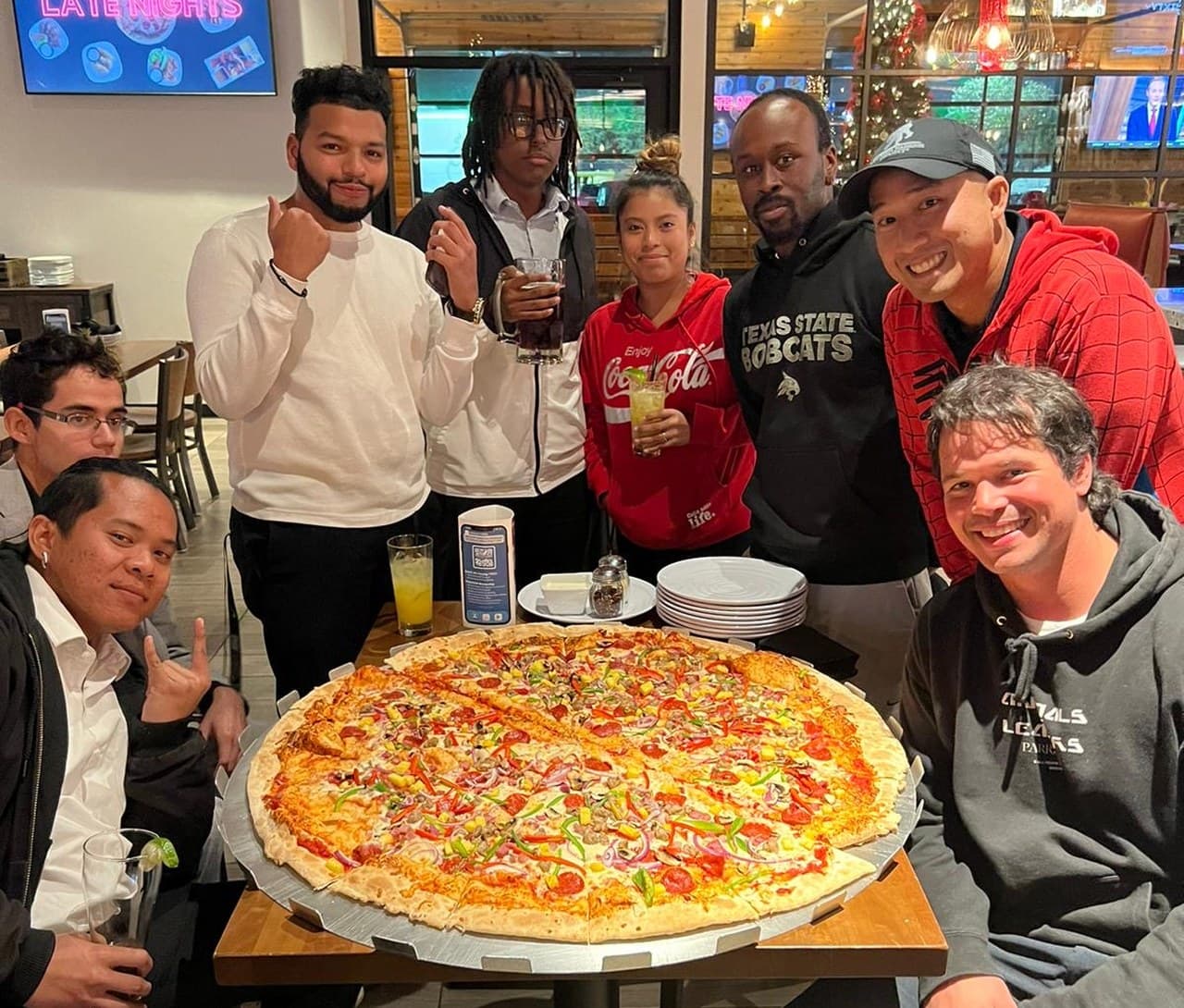 Eight teammates gathered around one giant pizza at a restaurant table.
