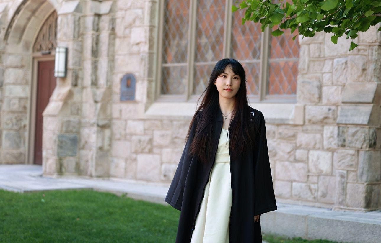 Xichen Mao in a graduation gown in front of a stone university building.