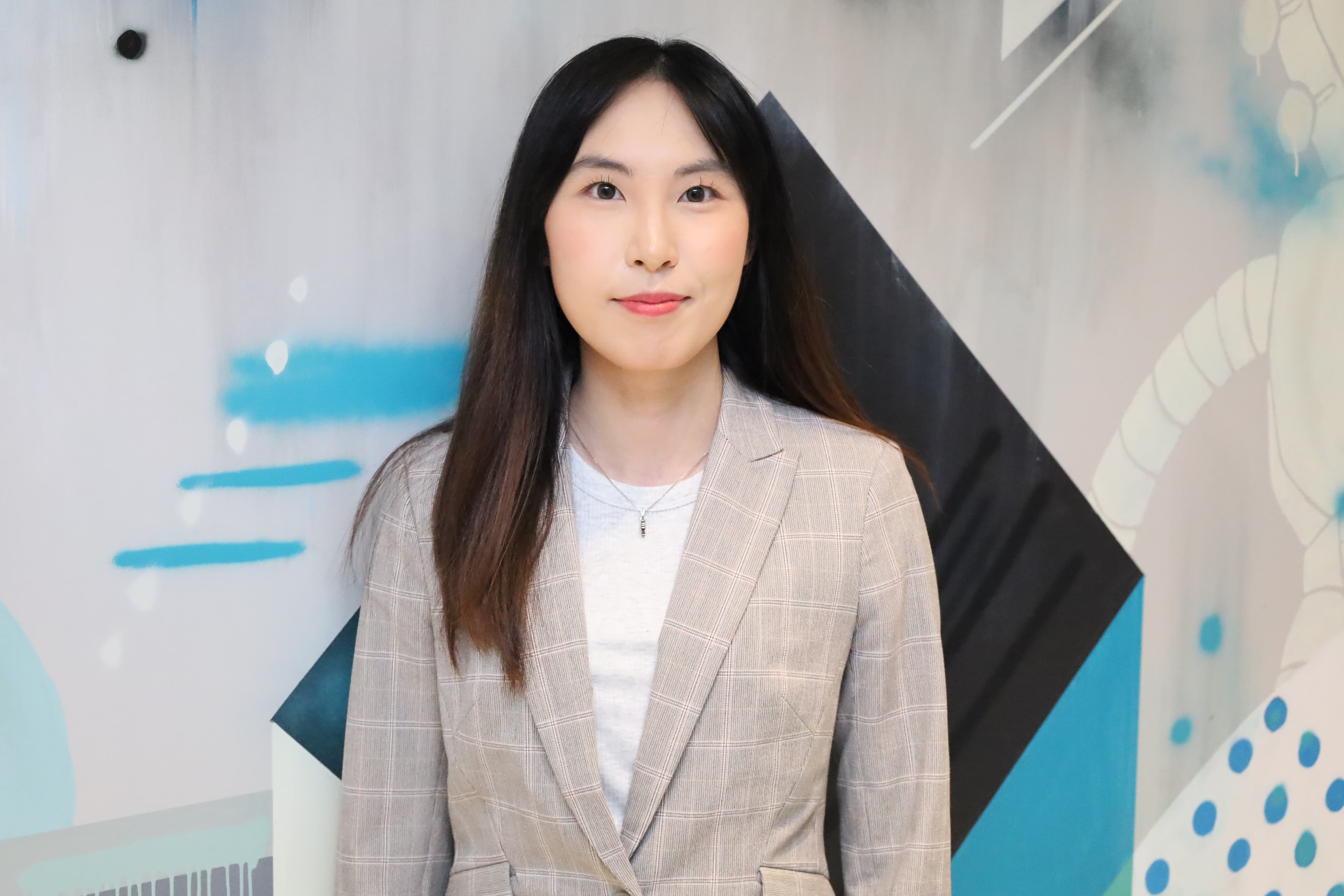 Portrait of Xichen Mao in a light blazer against a blue and charcoal mural