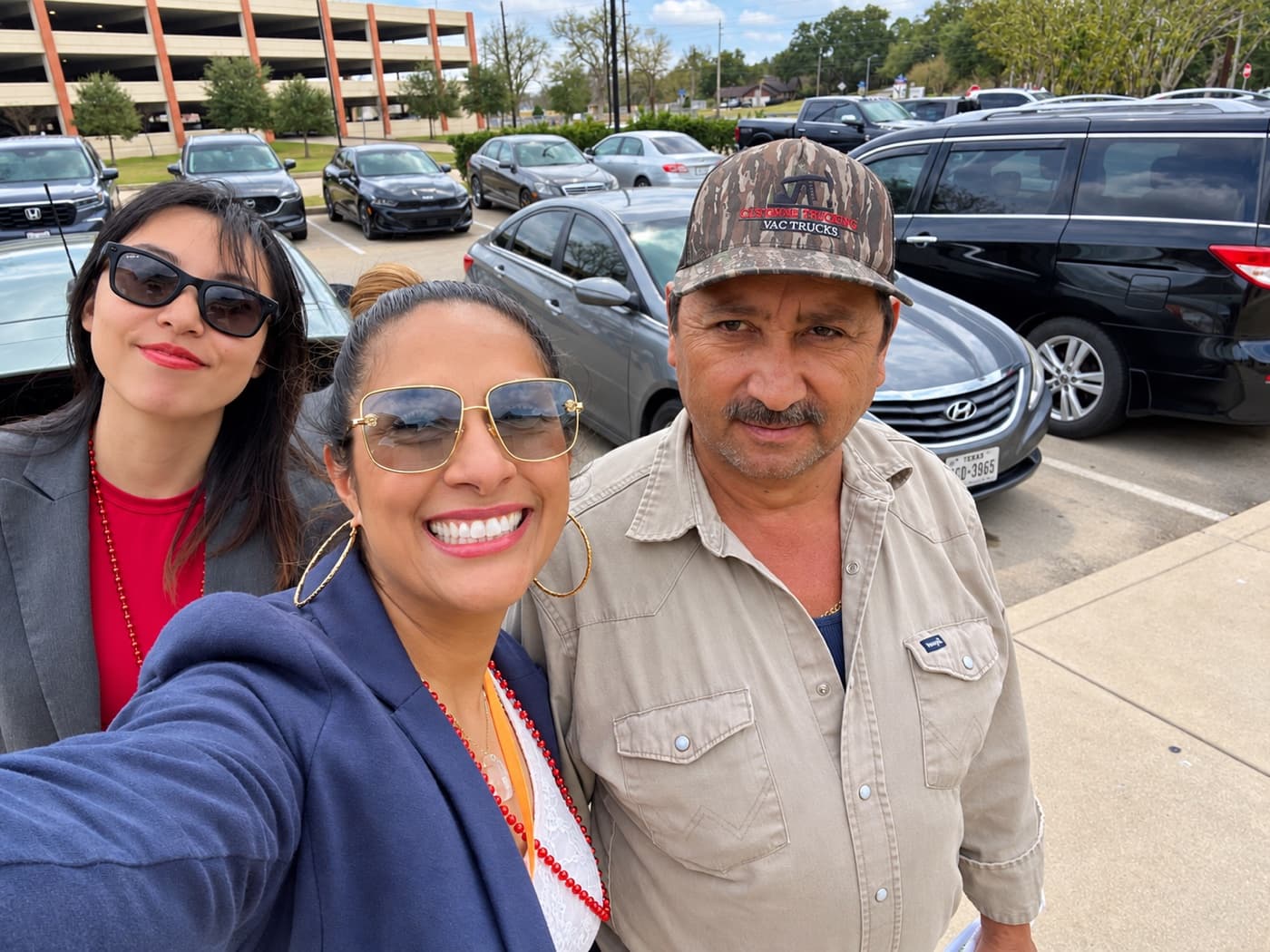 A fundraiser and two supporters in a parking lot on an overcast day