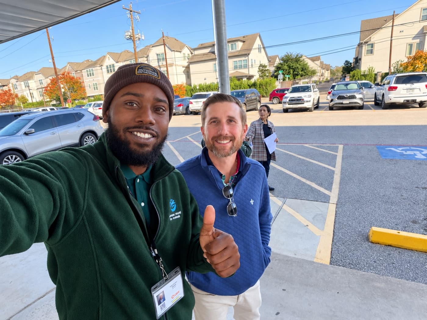 A fundraiser in a beanie and a supporter giving a thumbs up in a parking lot